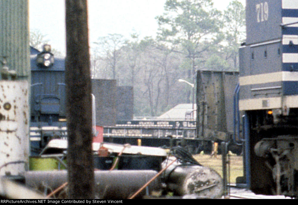 Extreme crop of some Apalachicola Northern pulpwood cars in background of loco photo.